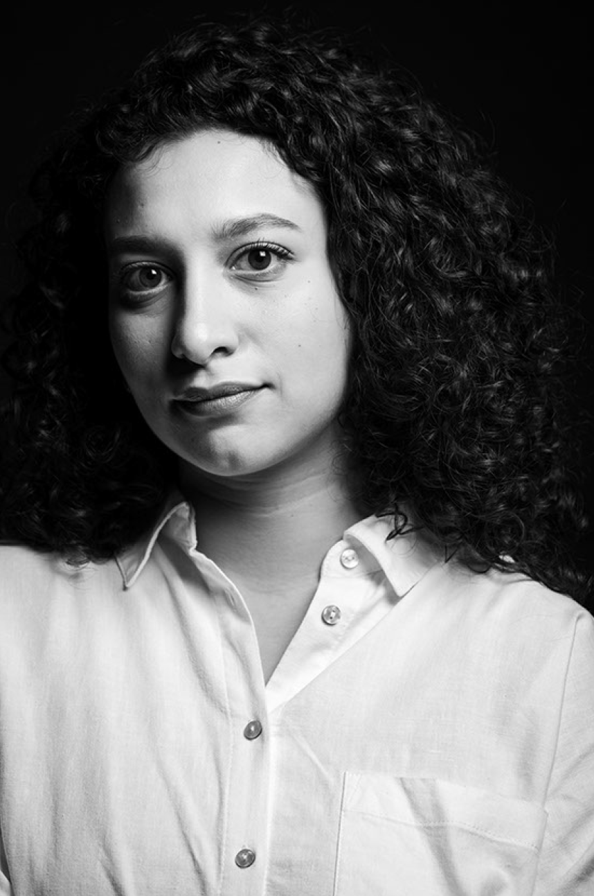Black and white portrait of a young woman with curly hair wearing a white button-up shirt, looking at the camera.