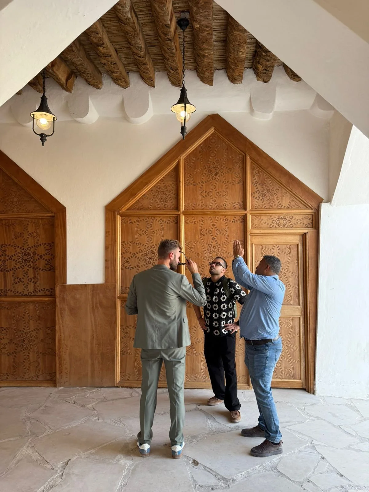 A modern multi-story building with a yellow spiral staircase outside, situated between two other apartment buildings, with palm trees in the background and a man riding a bicycle in the foreground.
