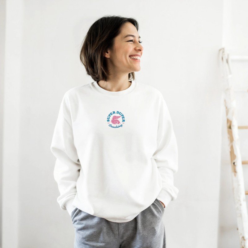 Une femme souriante portant un sweat blanc avec un logo coloré à l'avant, dans un intérieur lumineux.