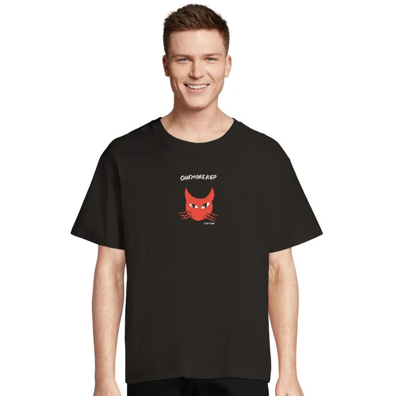 Jeune homme souriant portant un t-shirt noir avec un dessin d'un chat rouge et le texte « One More Rep ».