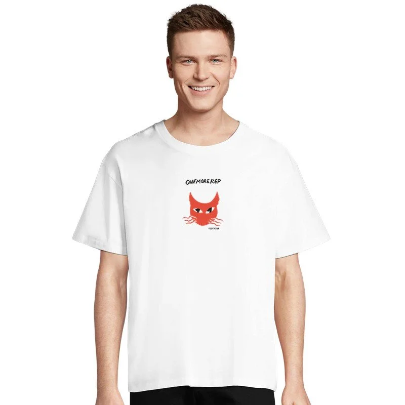 Jeune homme souriant portant un t-shirt blanc avec un dessin d'un chat orange et le texte 'ONEMOREREP' dessus.