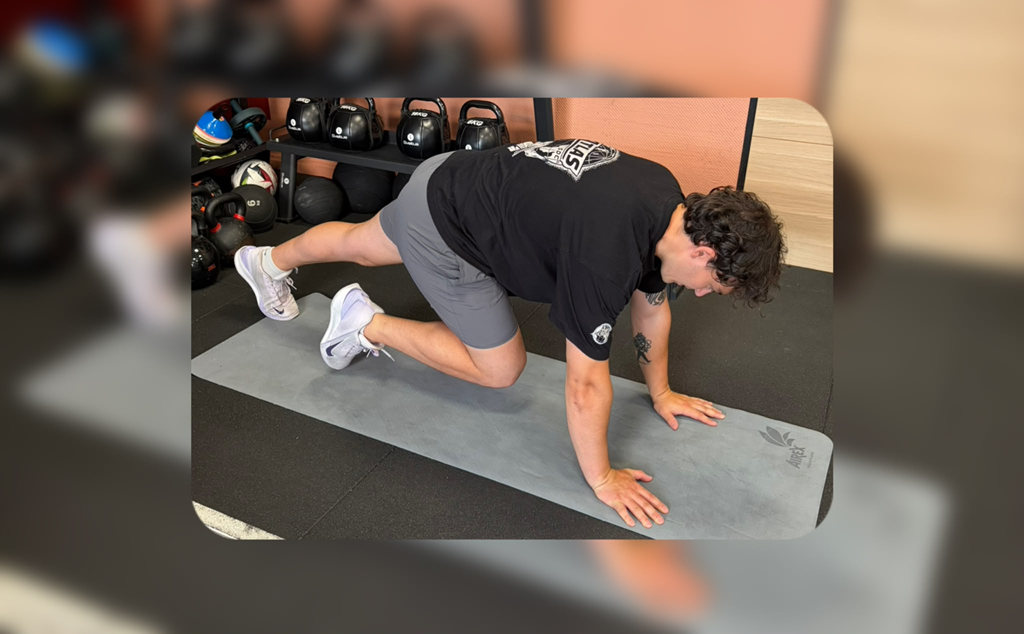 Une personne effectuant un exercice de planche avec un genou au sol sur un tapis de yoga dans une salle de sport.