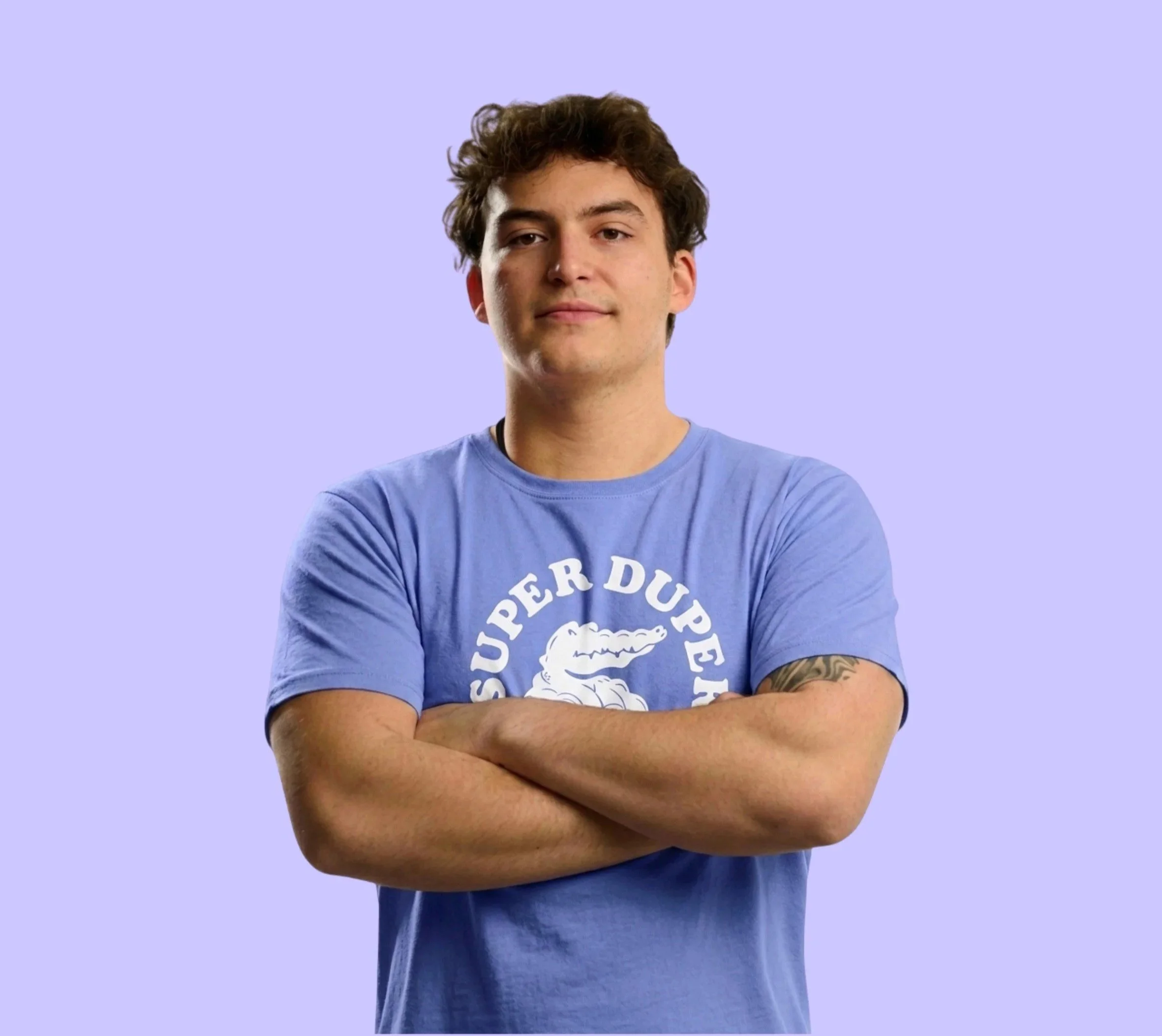 Jeune homme avec des bras croisés, portant un t-shirt bleu clair, fond violet