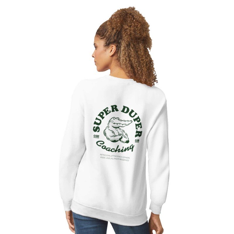 Une femme porte un sweat blanc avec un logo sur le dos représentant un crocodile et le texte « Super Duper Coaching ». Elle a des cheveux bouclés attachés en queue de cheval.