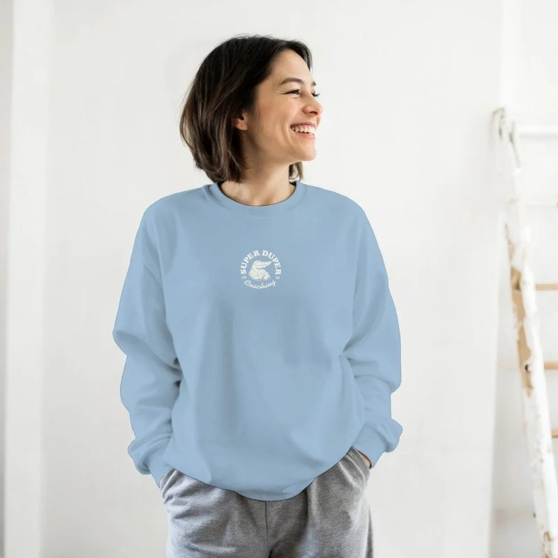 Femme souriante portant un sweat bleu clair avec un logo blanc, dans une pièce lumineuse.