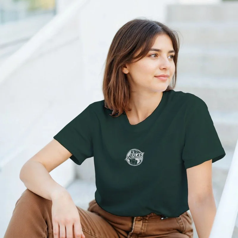 Une jeune femme aux cheveux bruns et aux yeux marrons, portant un t-shirt noir avec un logo Atlas, assise à l'extérieur sur un fond blanc et clair.