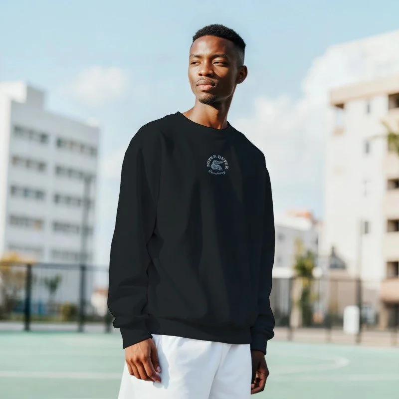Jeune homme debout sur un terrain de sport en plein air, portant un sweat noir et un pantalon blanc, avec un environnement urbain en arrière-plan.