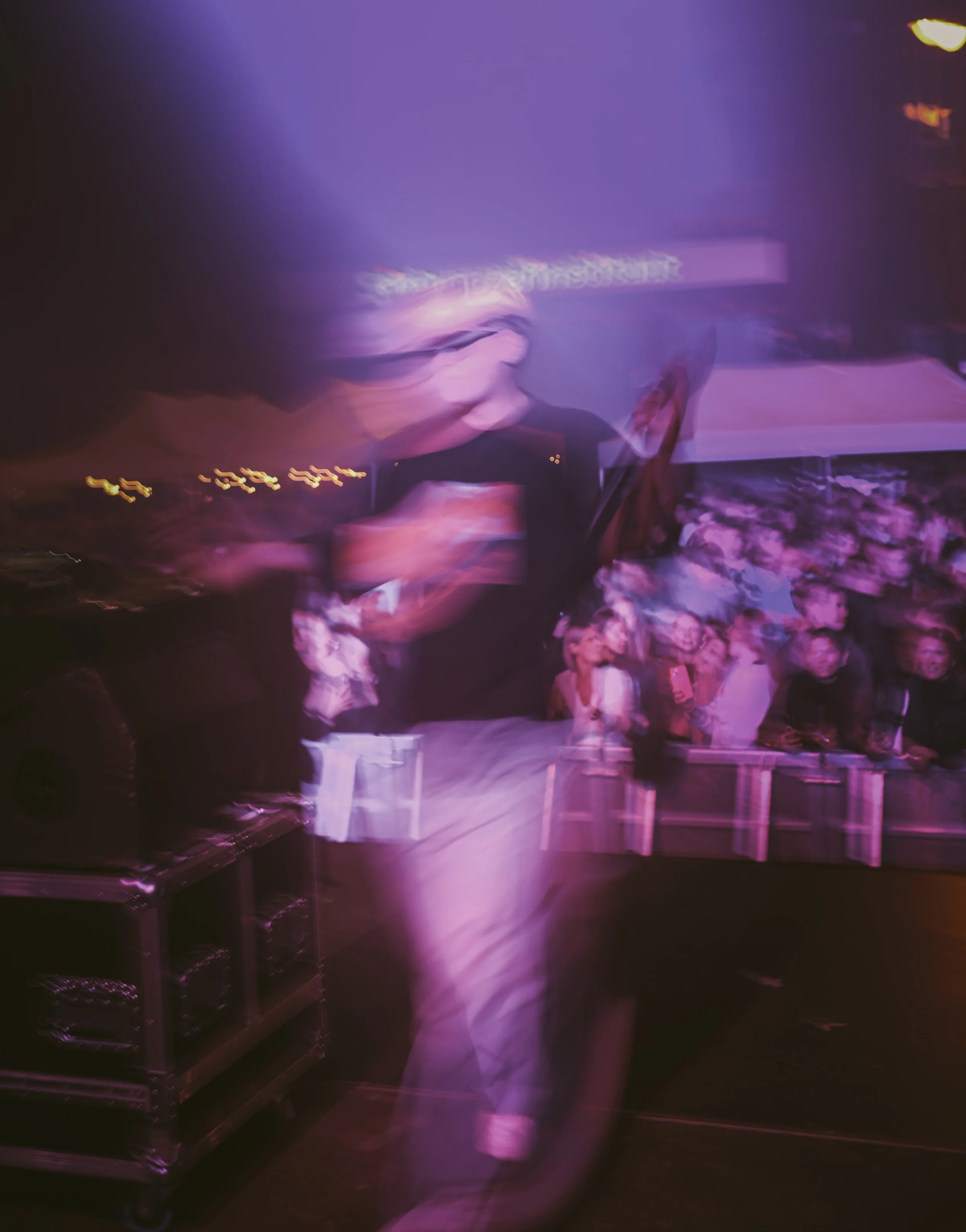 Blurred image of a person holding a smartphone at a lively event with a crowd watching.