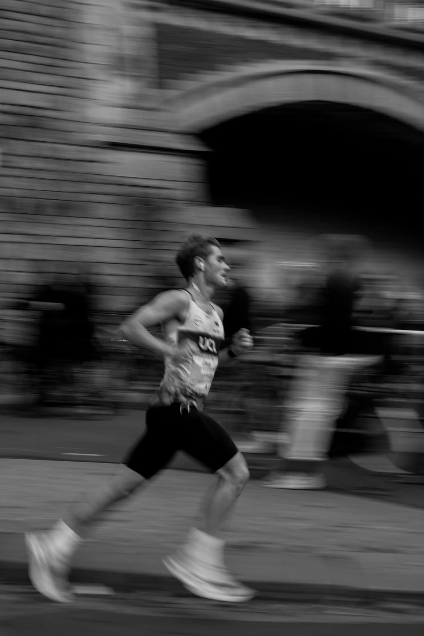 A person running in a race, captured in motion blur, with buildings and spectators in the background.