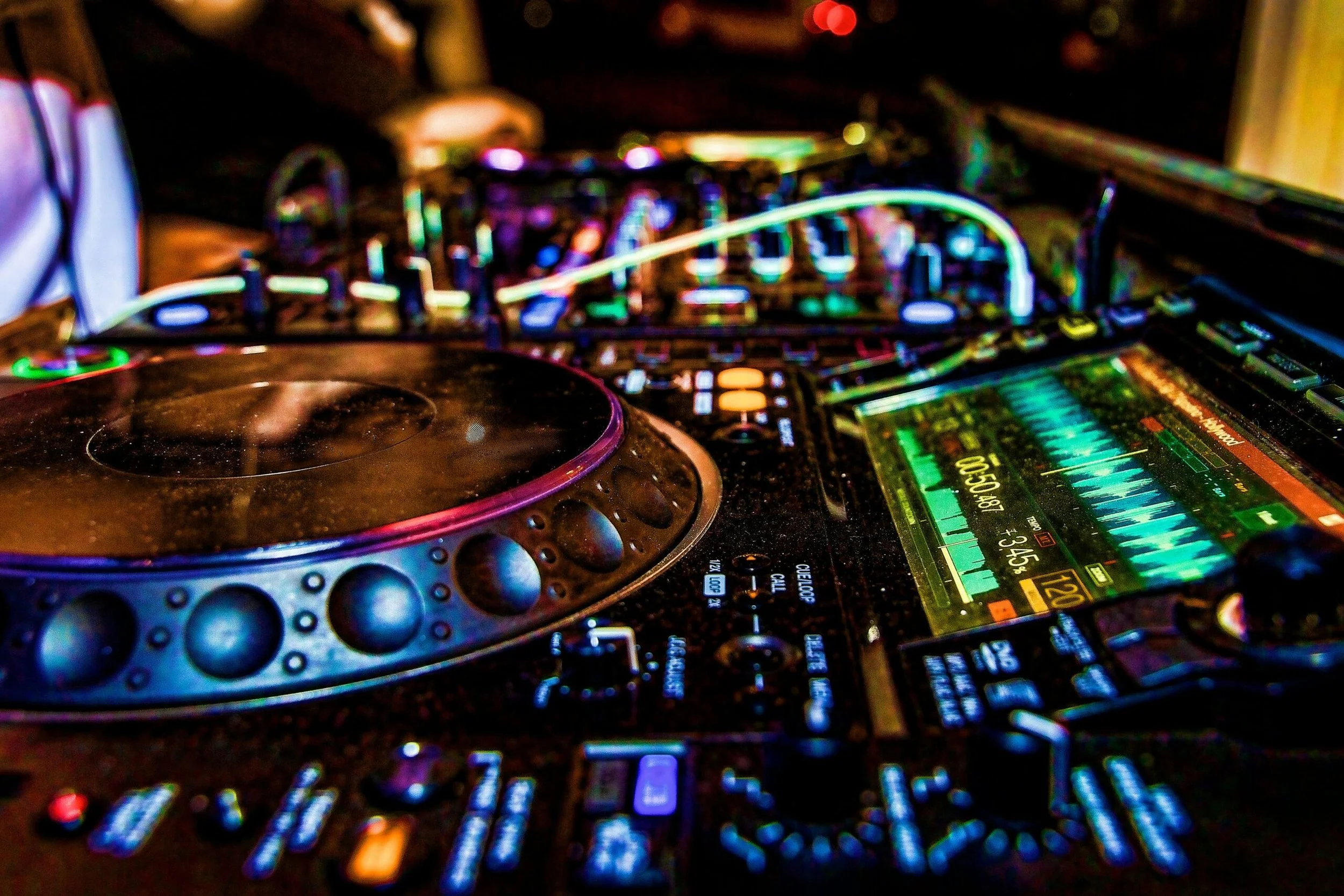 A DJ setup showing a turntable, mixer, and a tablet with colorful visualizations at a nightclub or party.