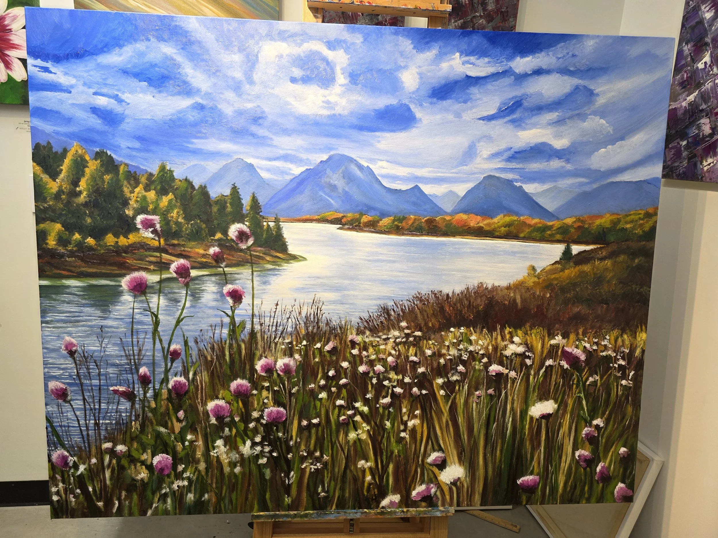 A landscape painting depicting a scenic view of a river flowing through mountains, with a cloudy blue sky, colorful trees, and pink and white wildflowers in the foreground.