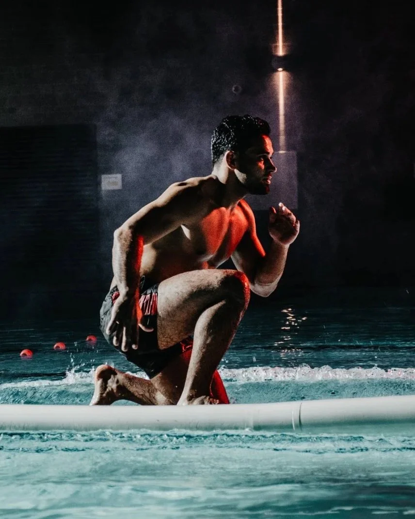 Man die op knieën in een zwembad staat, klaar om te zwemmen, met gespannen spieren en een donkere achtergrond.
