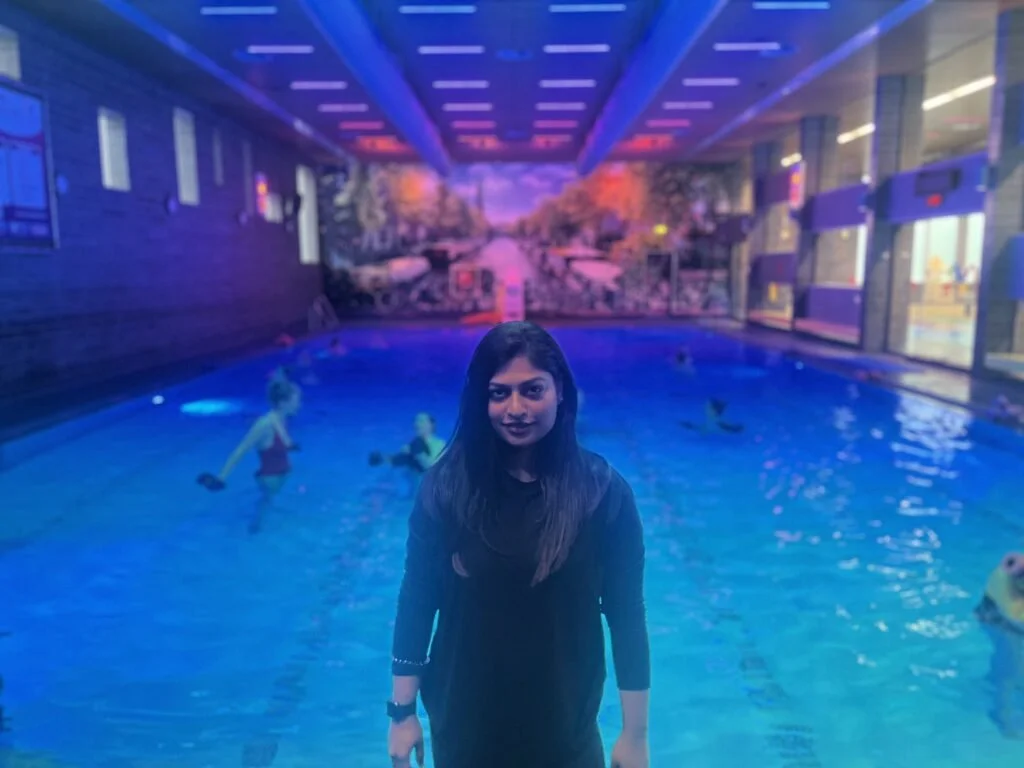 Vrouw in een binnenzwembad met neonverlichting en muurschildering op de achtergrond.