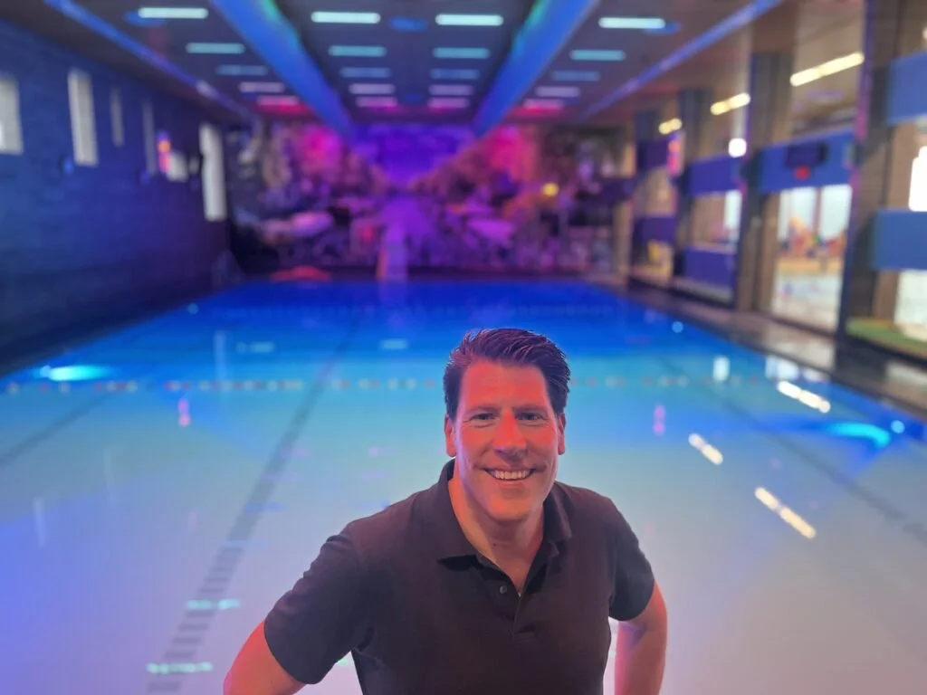 Man die in een zwembad staat met kleurrijke neonlichten in een indoor zwembadfaciliteit.