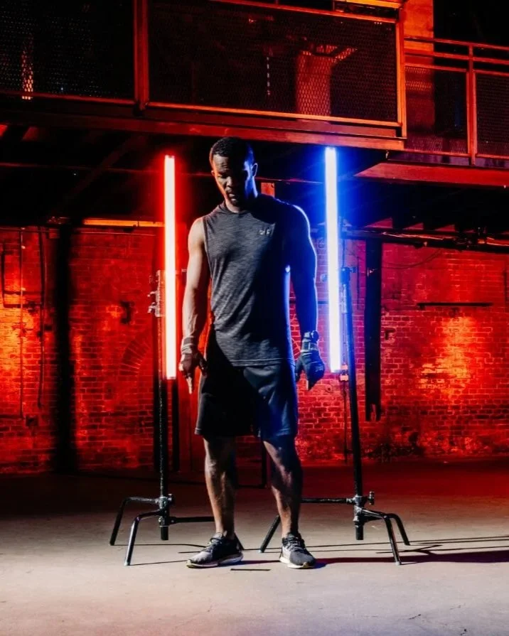 Een man in sportkleding met dumbbells in een ruimte met rode en blauwe neonlichten.