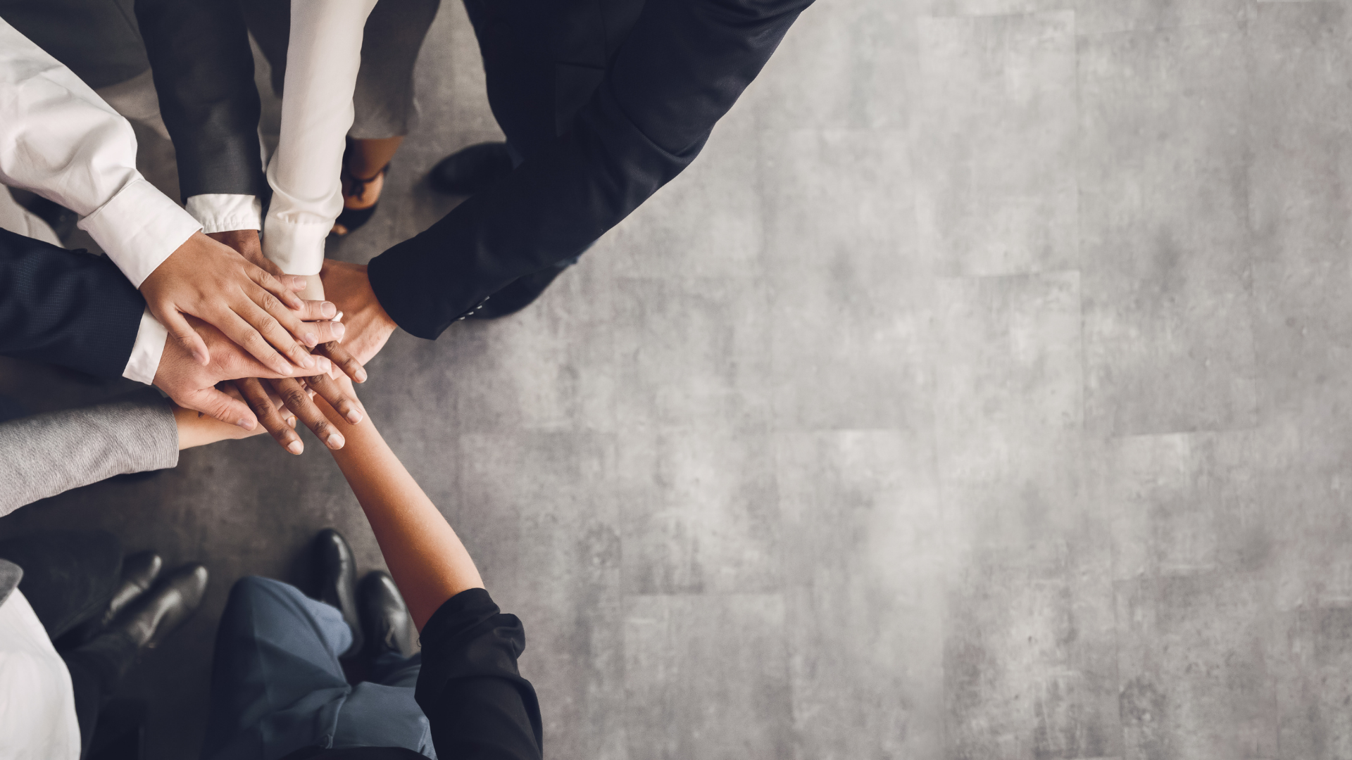 A group of diverse people in business attire putting their hands together in a show of teamwork.