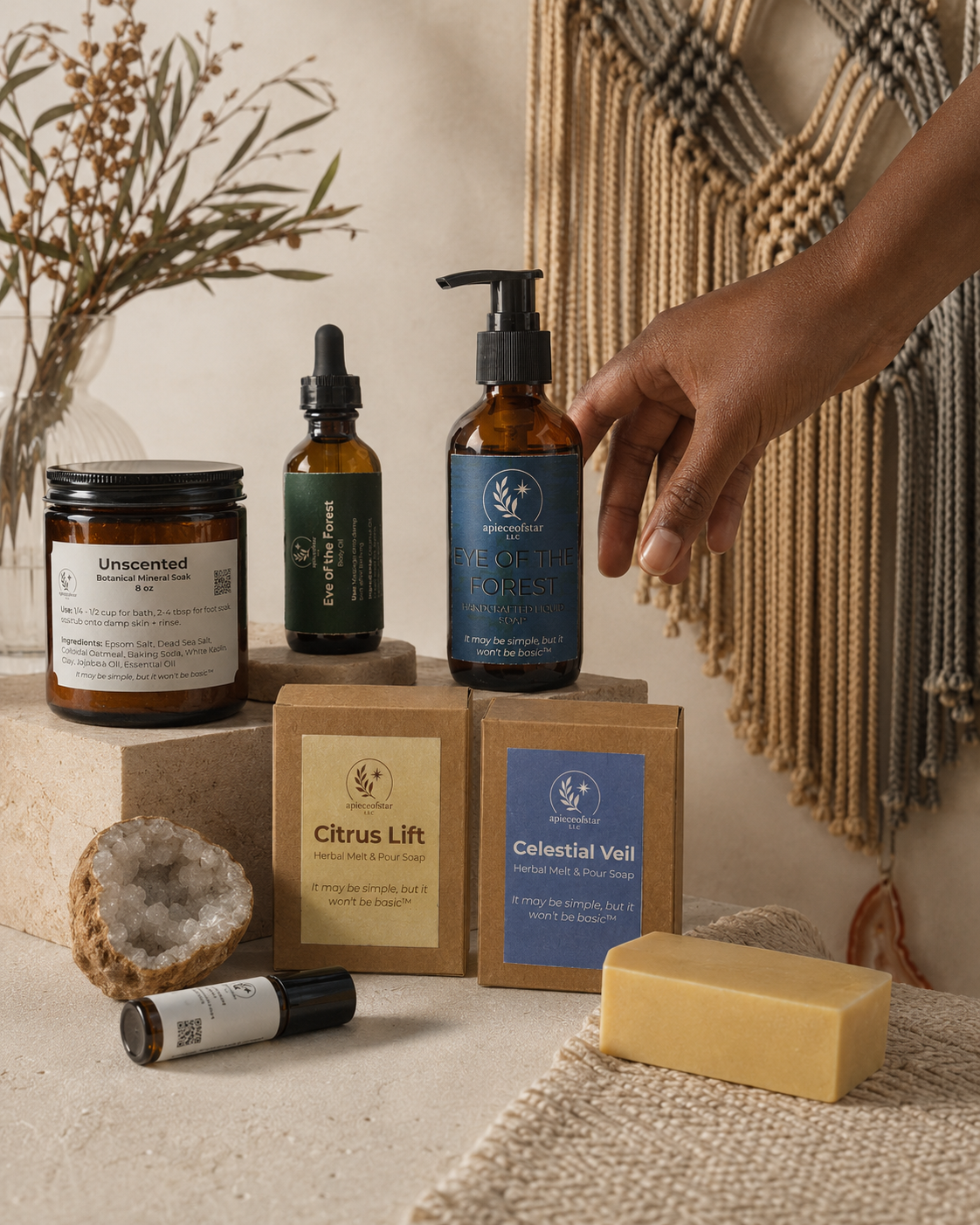 apieceofstar soaps, oils, mineral soak, crystals, and handmade adornments arranged on a textured surface beside macramé.