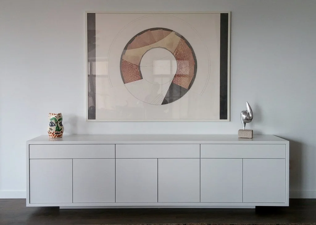A white sideboard against a white wall with abstract art hanging above, decorated with a colorful owl-patterned vase on the left and a metallic squirrel sculpture on the right.