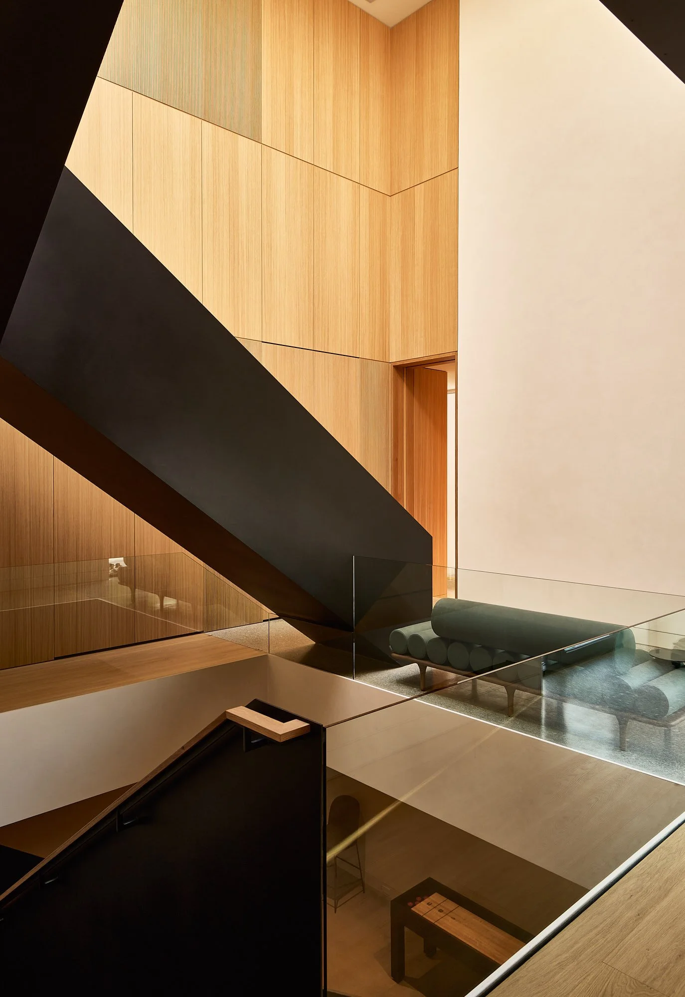 Modern interior with wooden paneling, black staircase, glass railing, and minimalist furniture.
