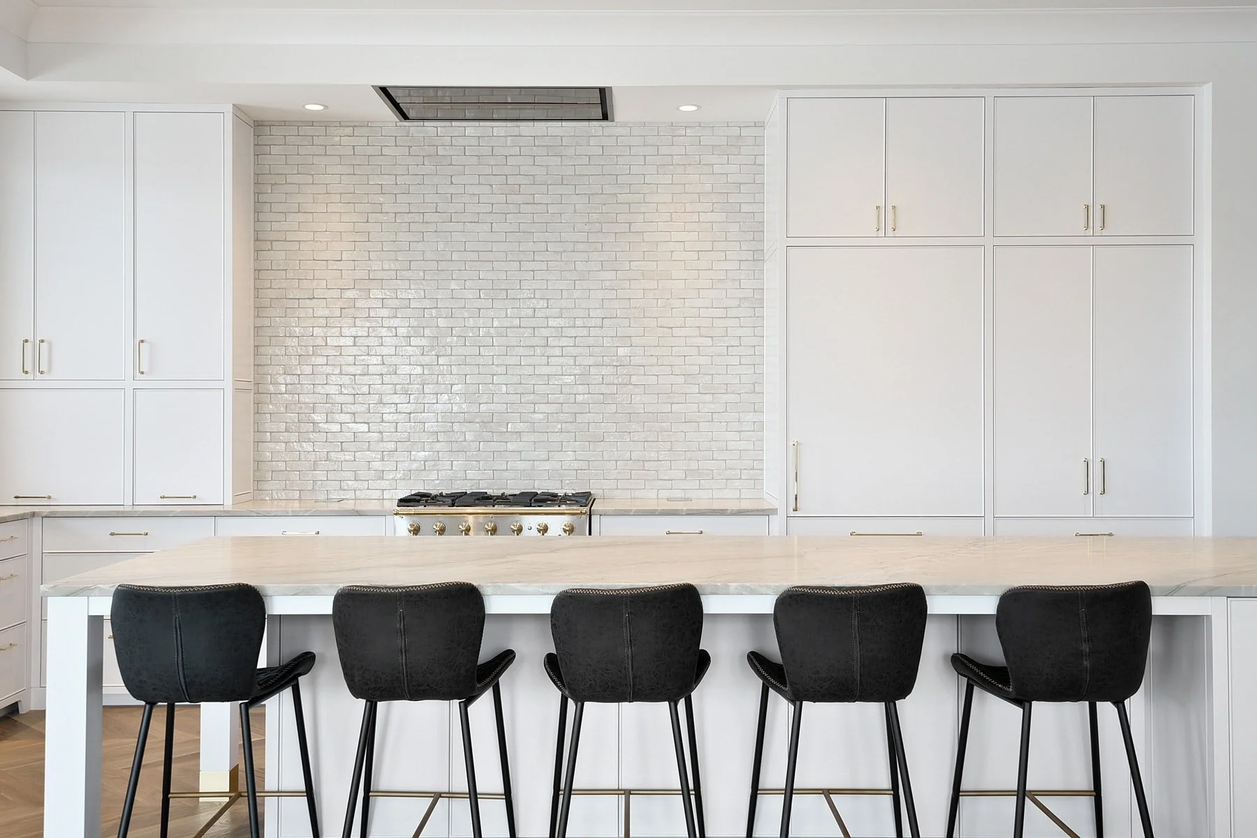 Modern kitchen with white cabinetry, white brick backsplash, gas stove, and black chairs at a white kitchen island.