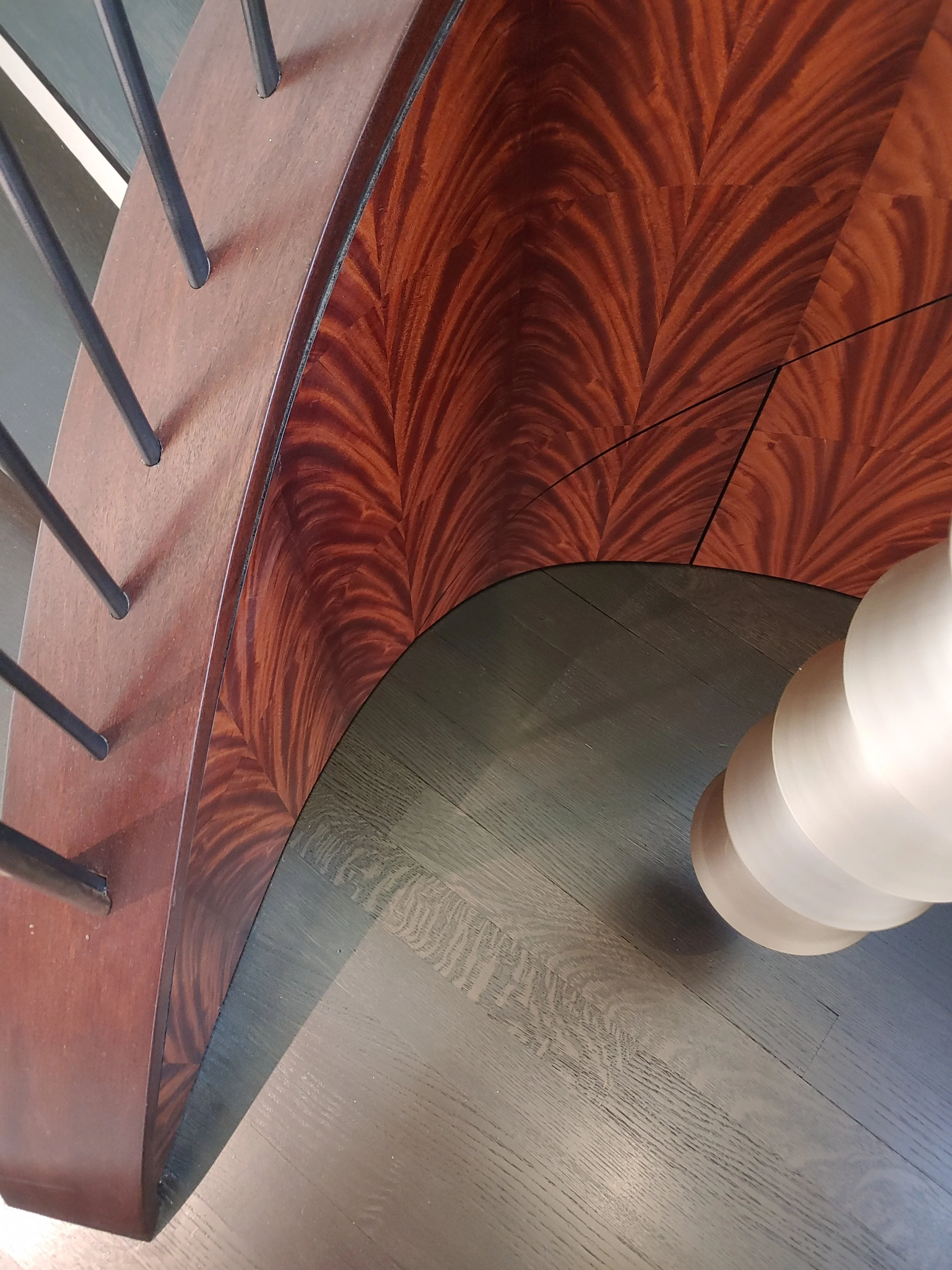 Close-up of a wooden cabinet with a rich, swirling grain pattern and three rounded, light-colored table legs nearby. Part of a wooden floor is visible beneath.