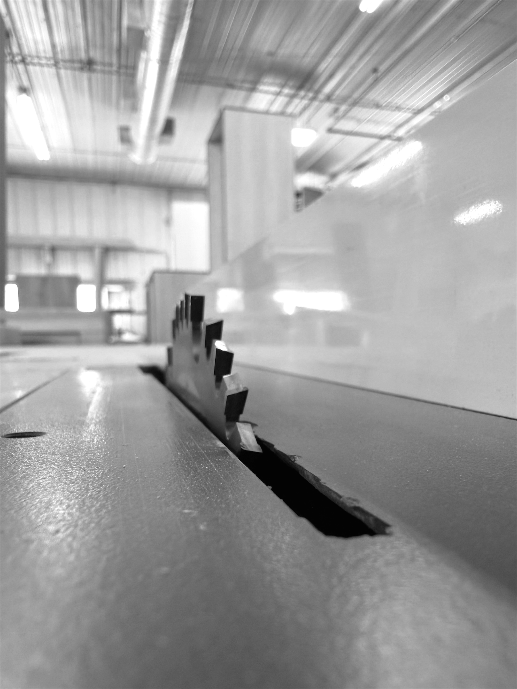 Close-up of a table saw blade with a woodworking square and a metal tool in a workshop setting.