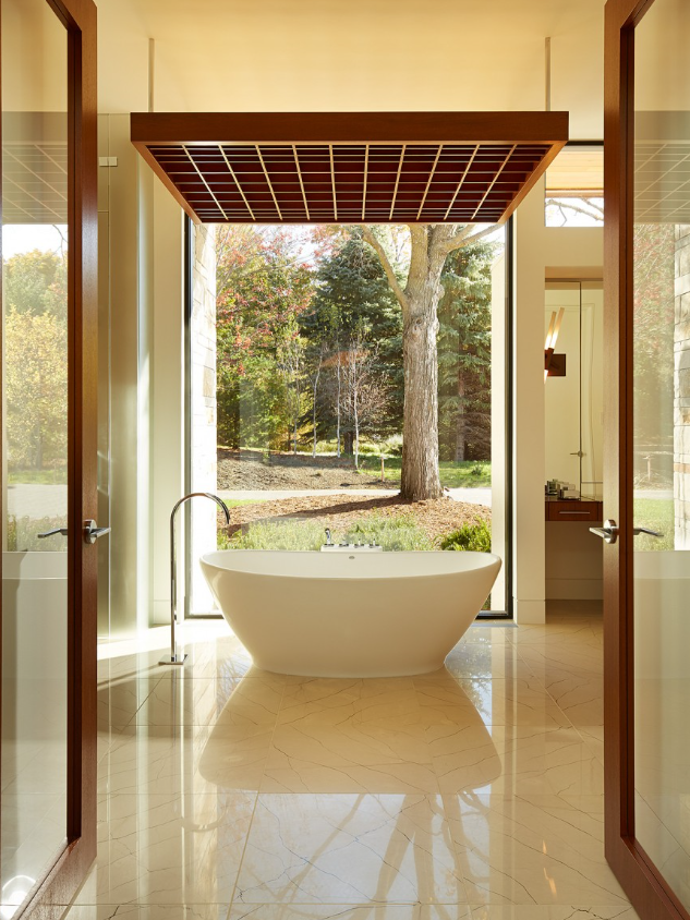 Modern bathroom with a freestanding bathtub placed in front of a large window showing trees and greenery outside.