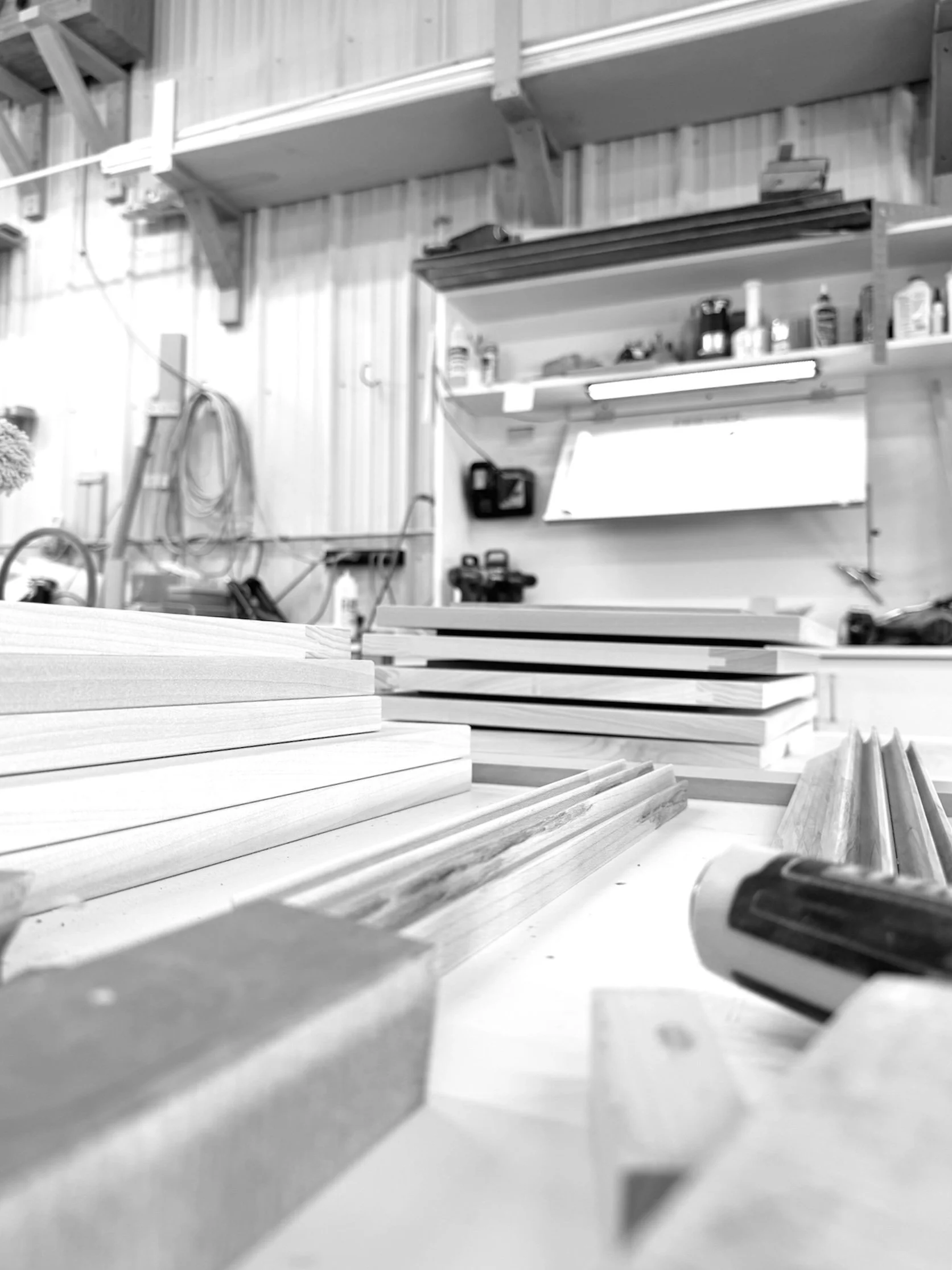 Craftsmanship at work, wood pieces on a workbench in a woodworking shop with shelves containing tools and supplies in the background.