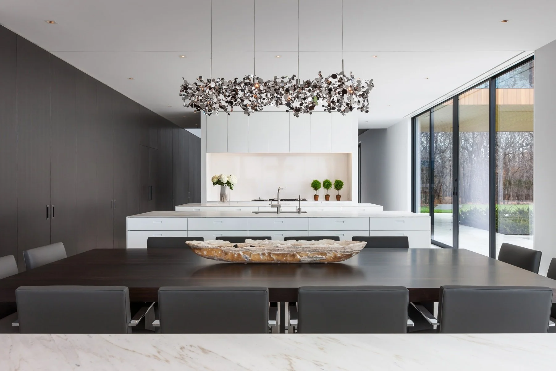 Modern kitchen with white cabinetry, black wall, large window, and black dining chairs around a dark wood table with a decorative centerpiece.