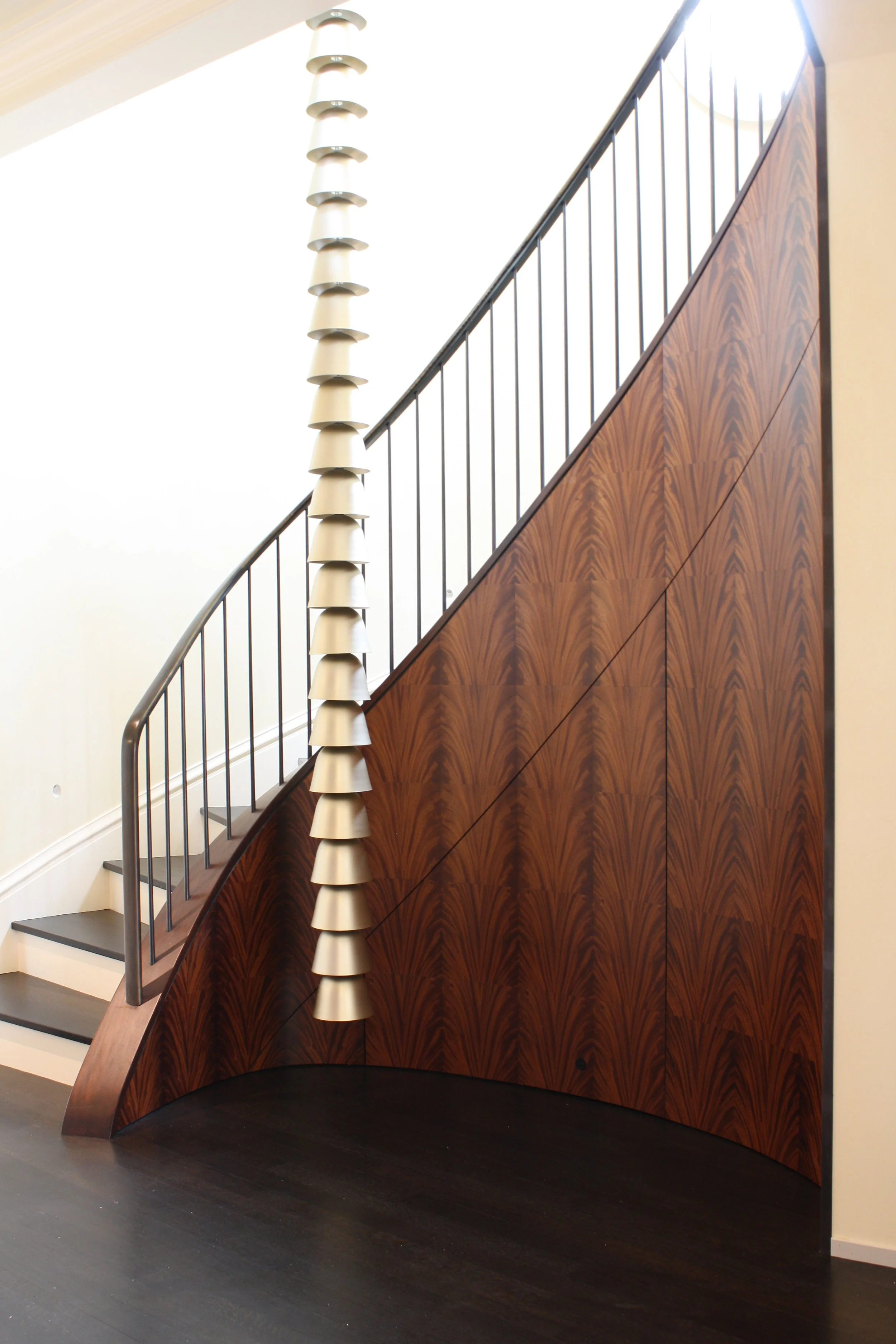 Interior view of a staircase with dark wood paneling and a unique decorative side feature resembling stacked bowls or bells, with black metal handrails and gray steps.