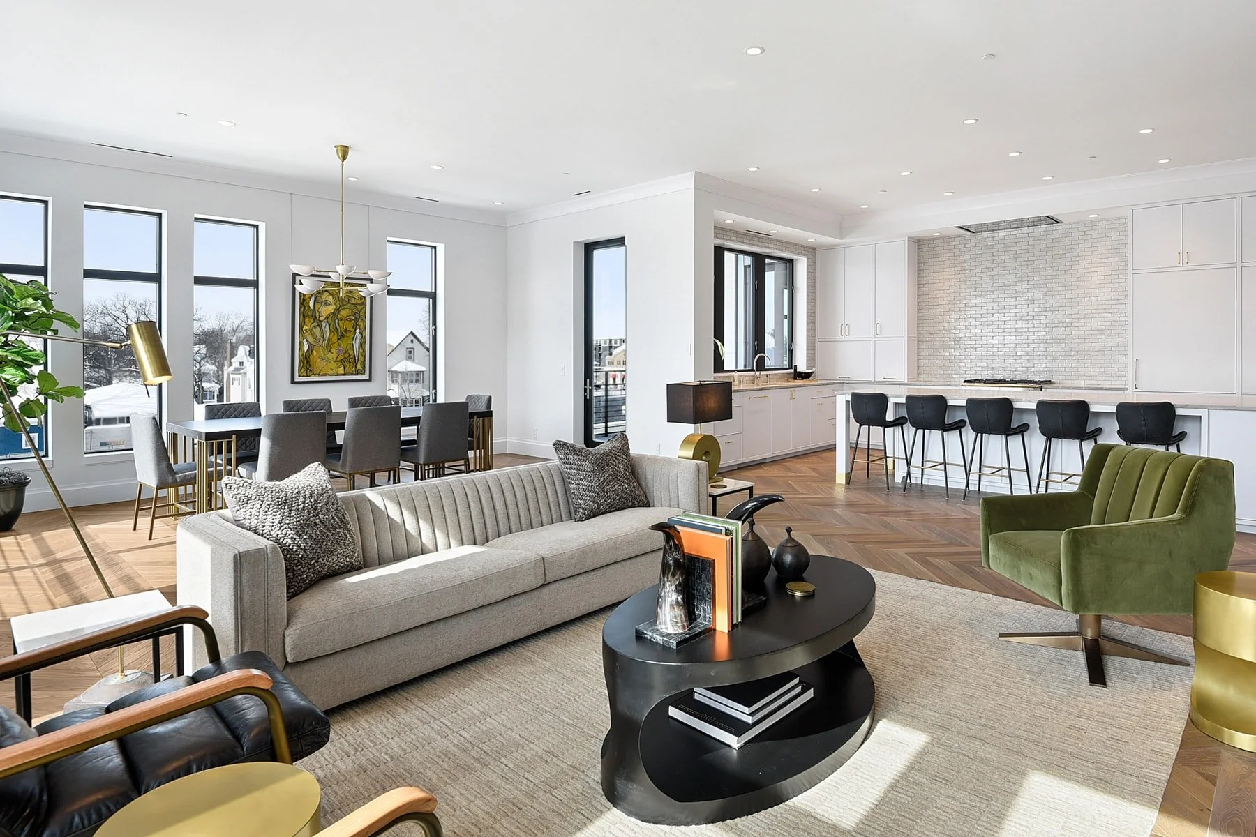 Open-concept living room and kitchen with large windows, modern furniture, and hardwood floors.