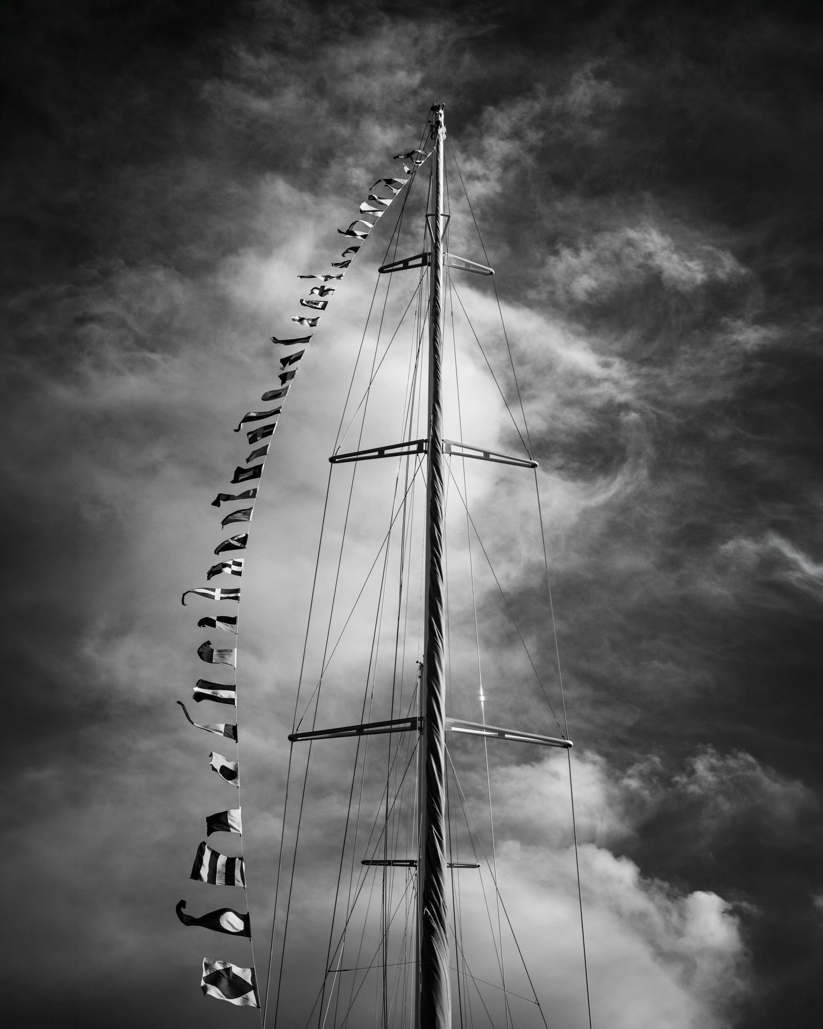 Sailboat mast and signal flags against a cloudy sky black and white fine art photography print, nautical Nordic study