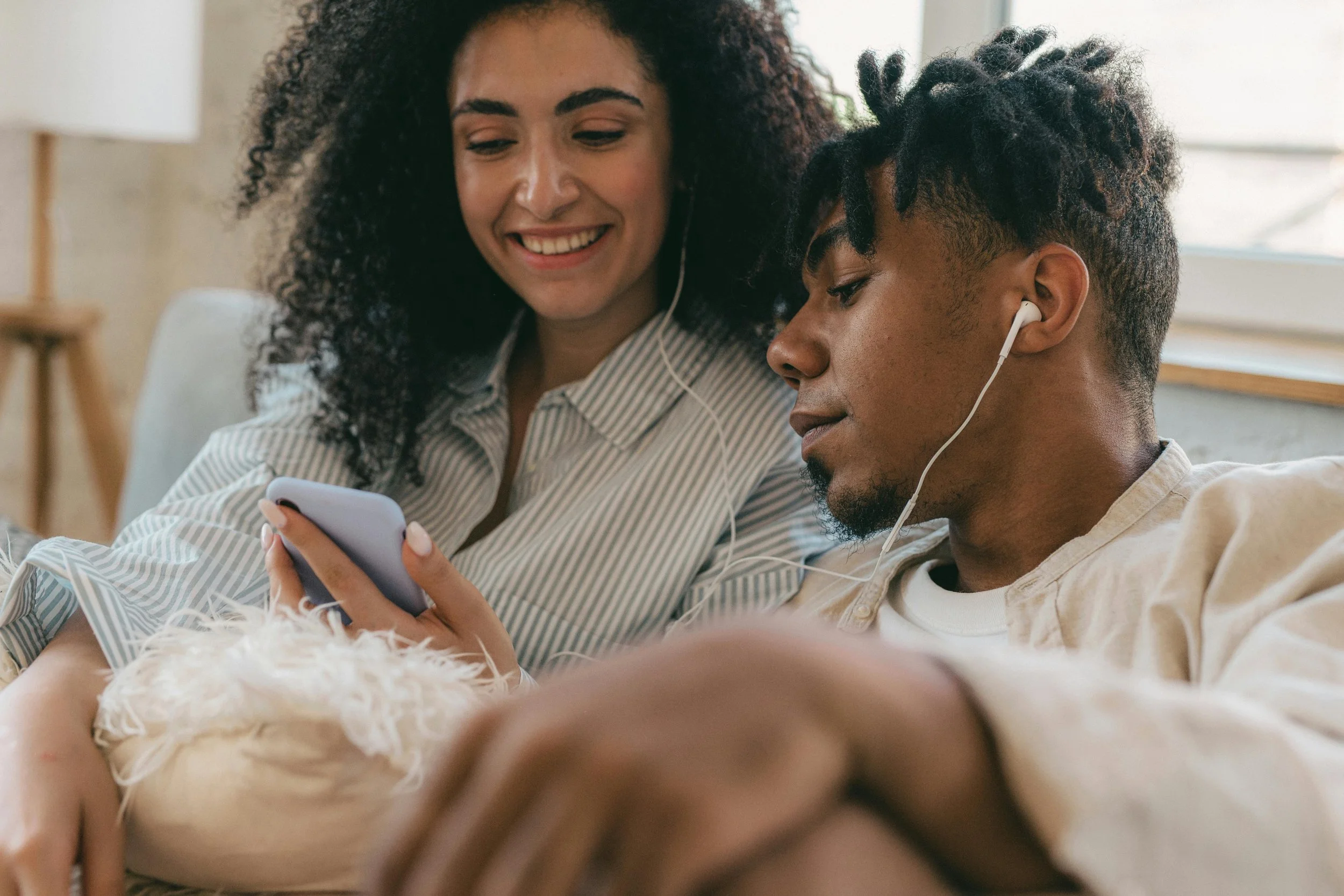 Man sitting on a couch sharing headphones with his partner, symbolizing connection, safety, and healing through trauma therapy in California.