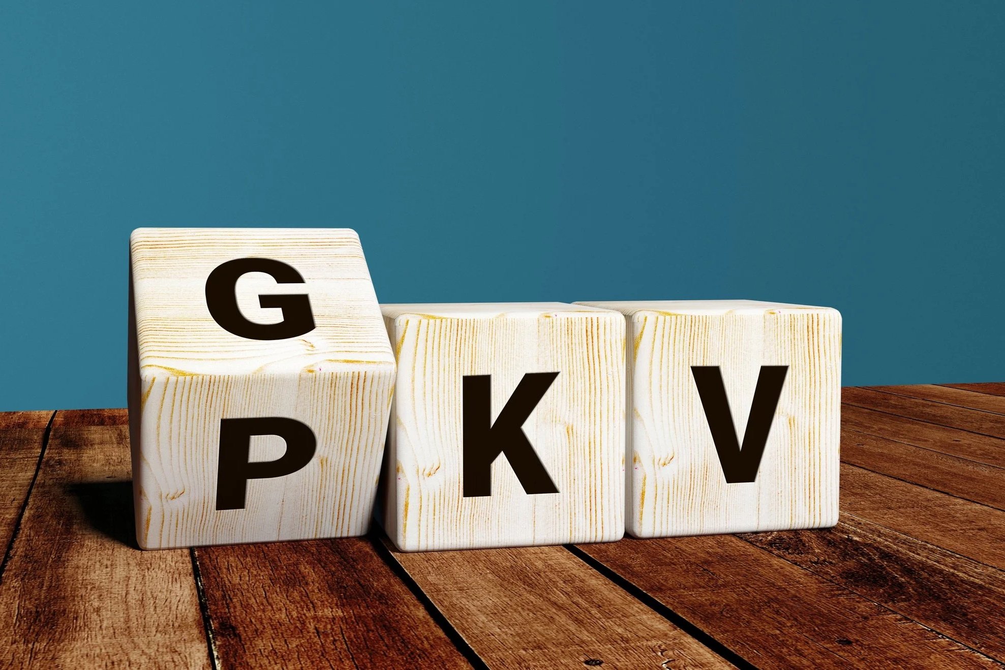 Vier Holzklötze mit schwarzen Buchstaben G, P, K, V auf einer Holzoberfläche gegen blauen Hintergrund
