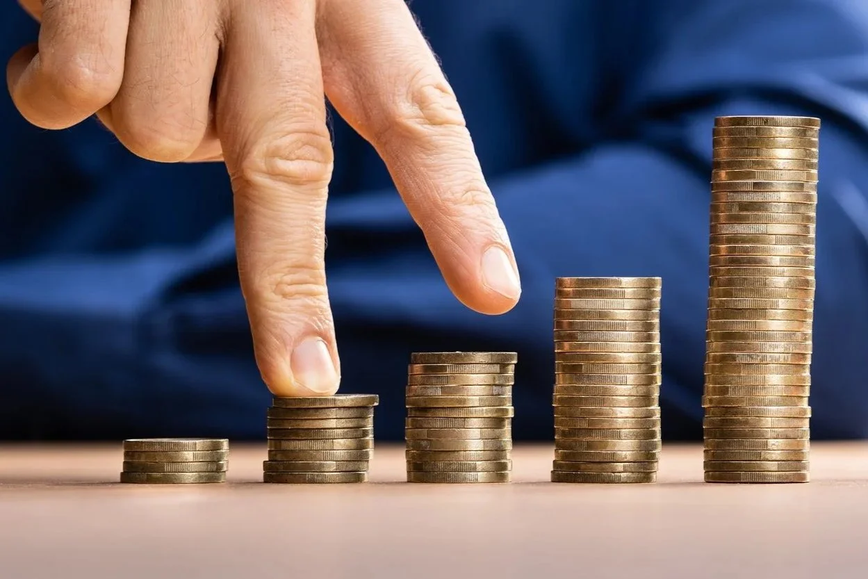Eine Hand stapelt Münzen in aufsteigender Höhe, die die Steigerung von Geld oder Wachstum symbolisieren.