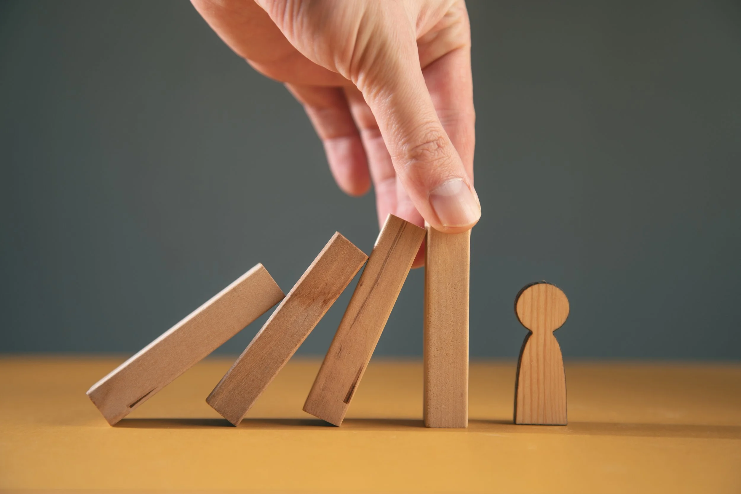 Hand hebt einen Holzblock an, um eine Reihe von fallenden Holzblöcken zu stoppen, neben einer Holzfigur auf einem Tisch.