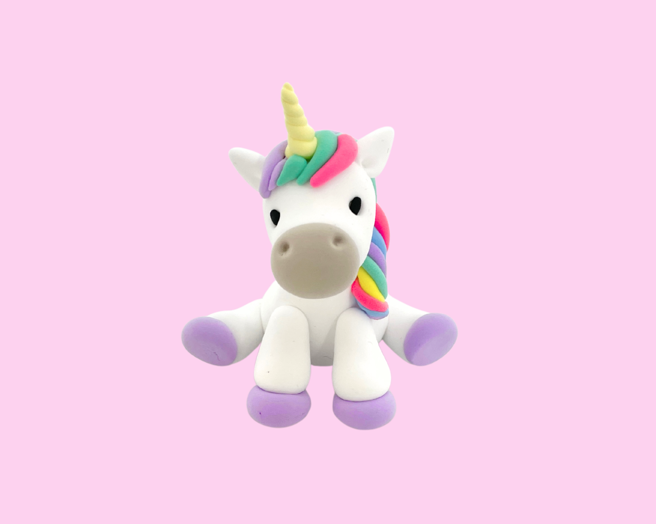 Colorful plush unicorn toy with a rainbow-colored mane and tail, sitting against a pink background.