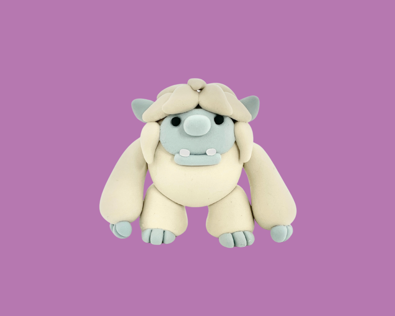 A handmade clay sculpture of a cartoonish mammoth with light gray face and tusks, beige body, and gray horn and claws, set against a purple background.