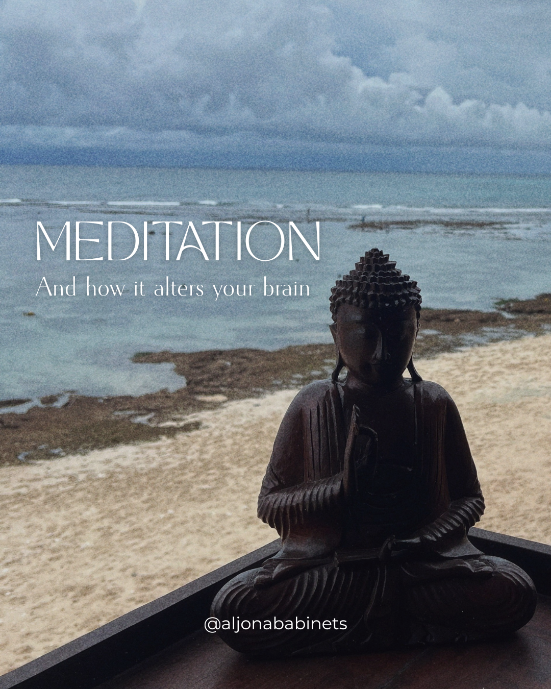 A wooden Buddha statue sitting on a table near the beach with the ocean and cloudy sky in the background.