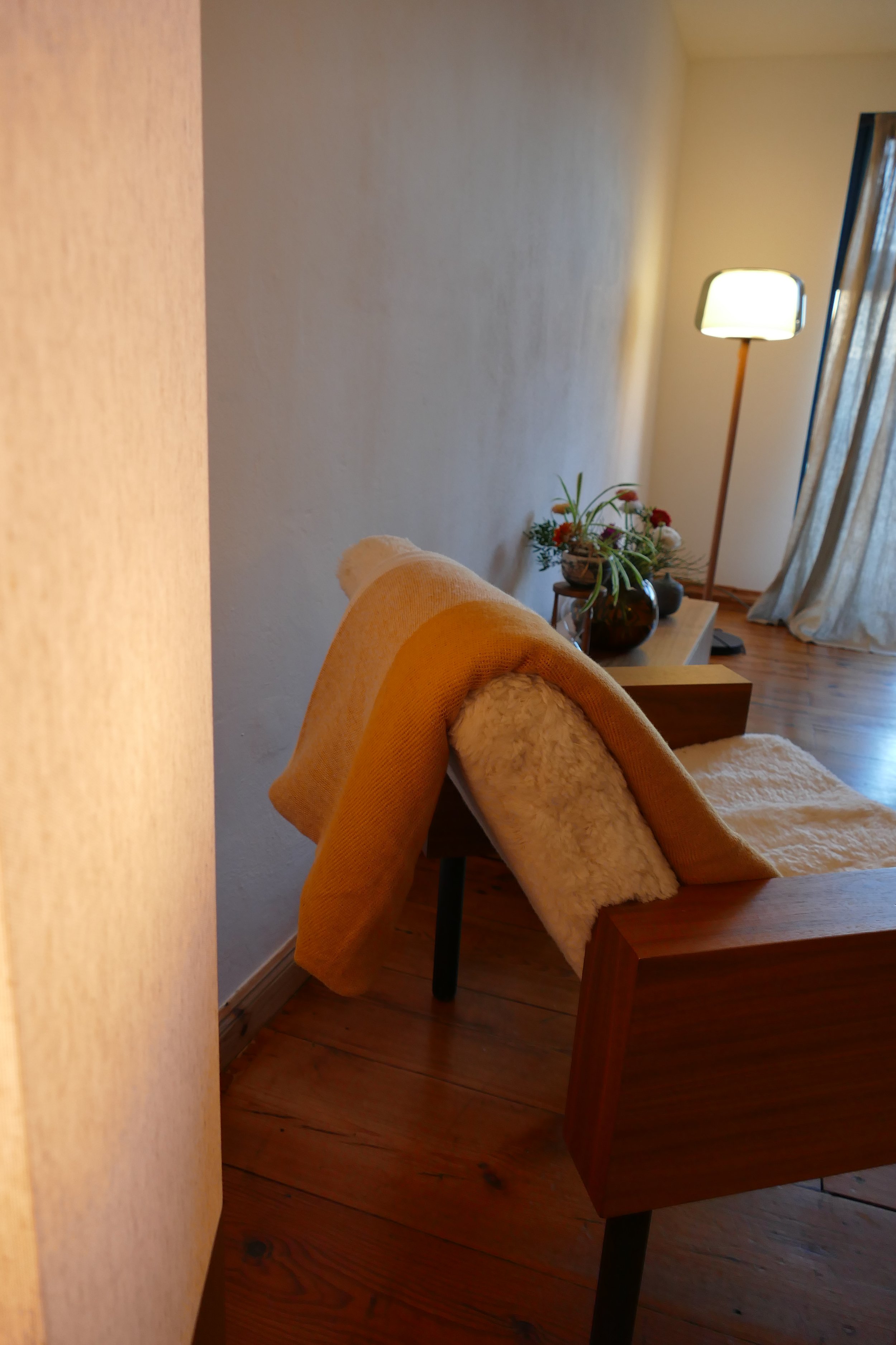 Der Therapie-Raum mit einem hellen Sessel, einem Blumentopf mit bunten Blumen und einer gemütlichen Decke.