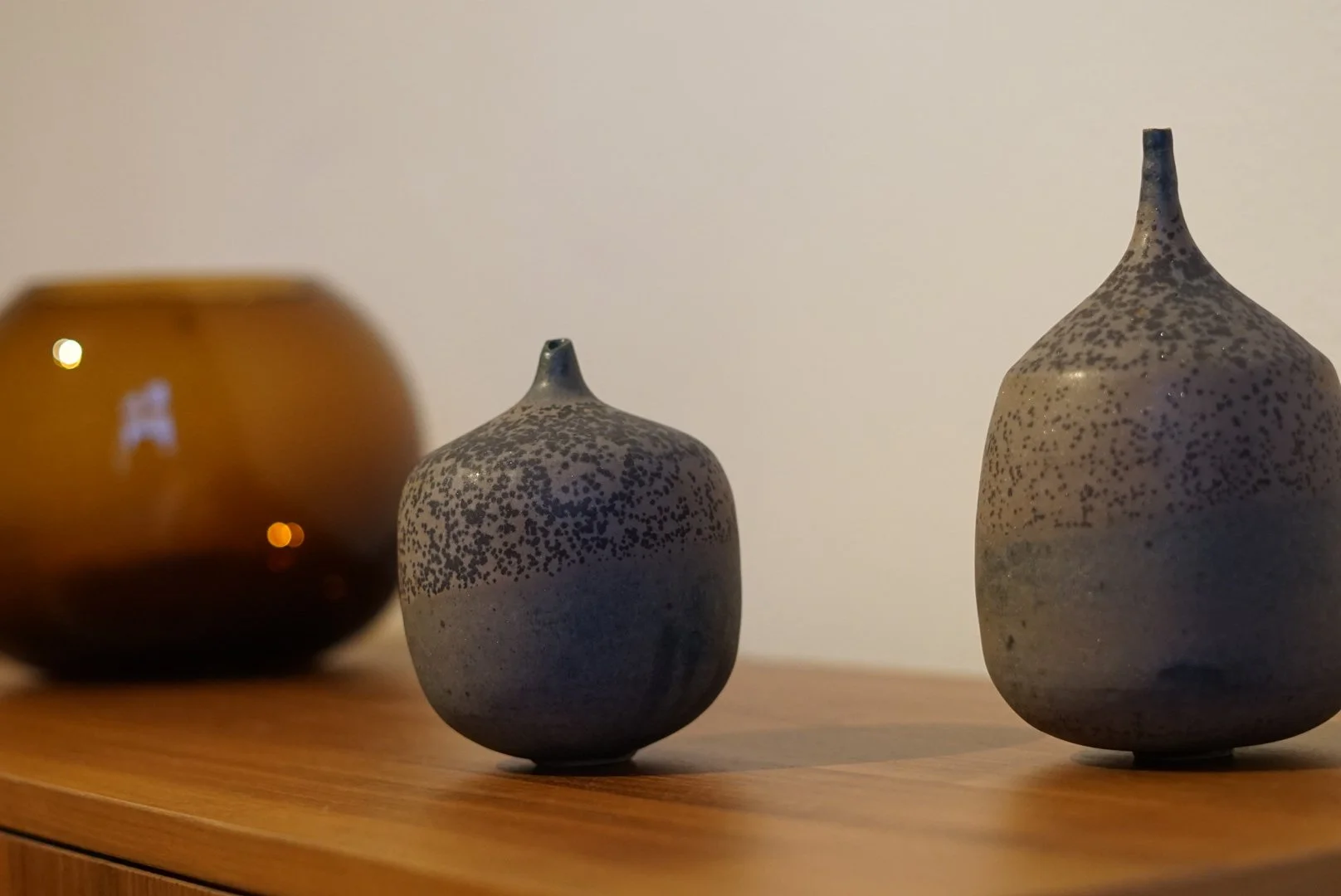 Drei dekorative Keramikvasen in verschiedenen Größen und Farben auf einem Holzregal.