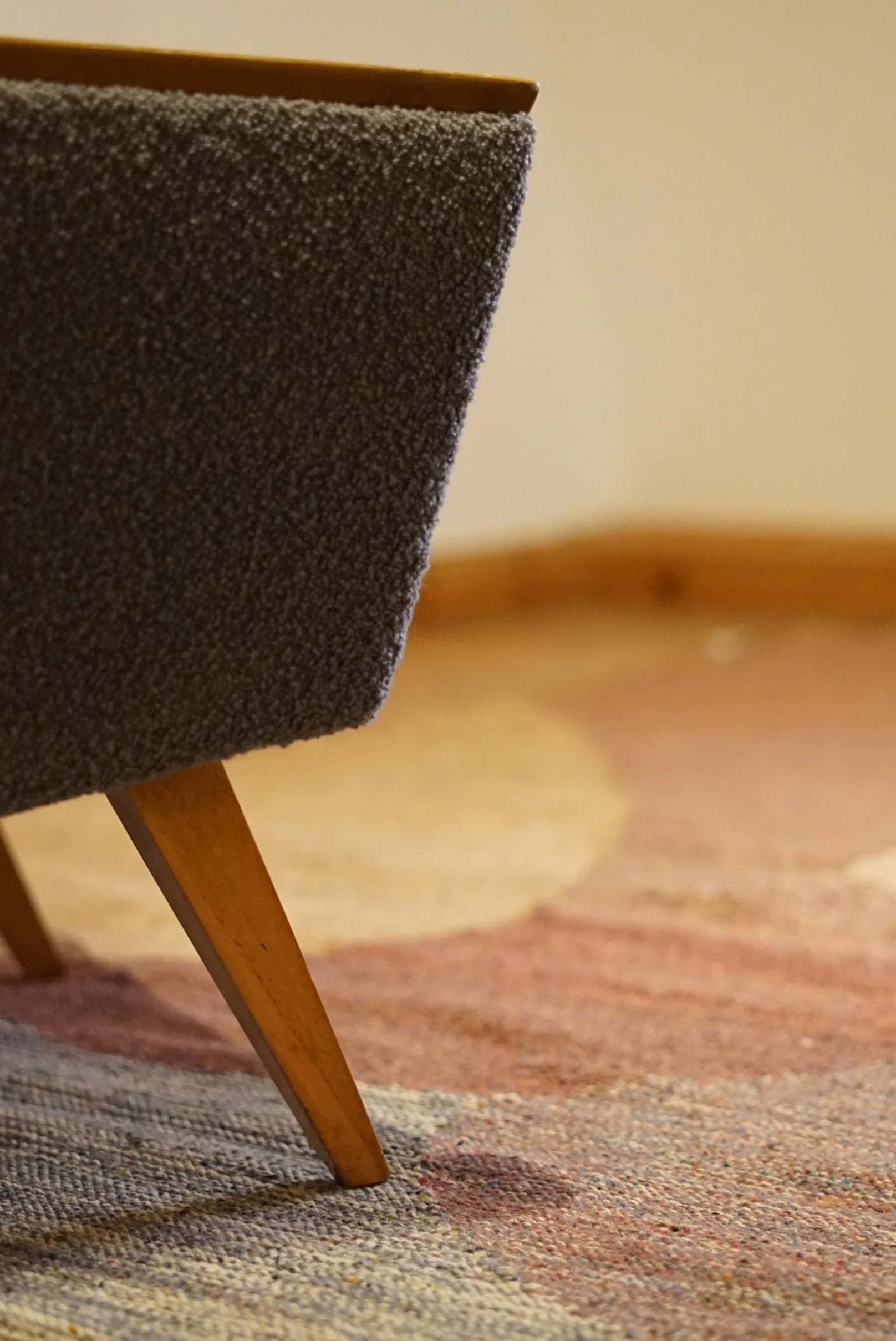 Ein Sessel mit einem holzfarbenen Rahmen und einem grauen Stoffbezug, der auf einem bunten Teppich steht.