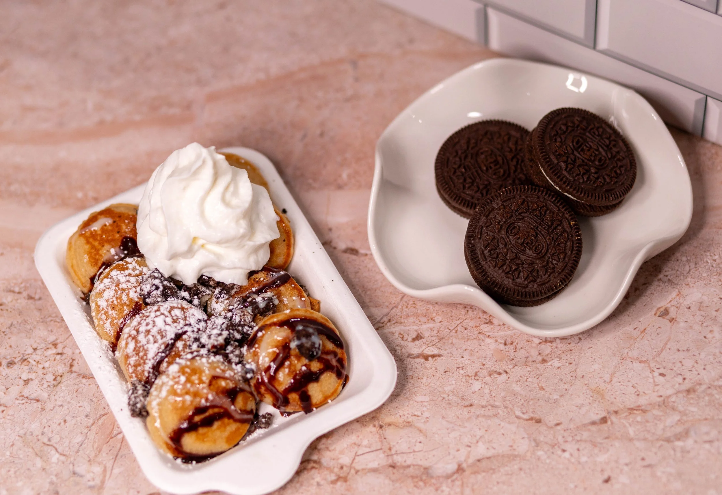 Plate of mini donuts topped with powdered sugar, whipped cream, and caramel sauce, alongside a dish of Oreo cookies.