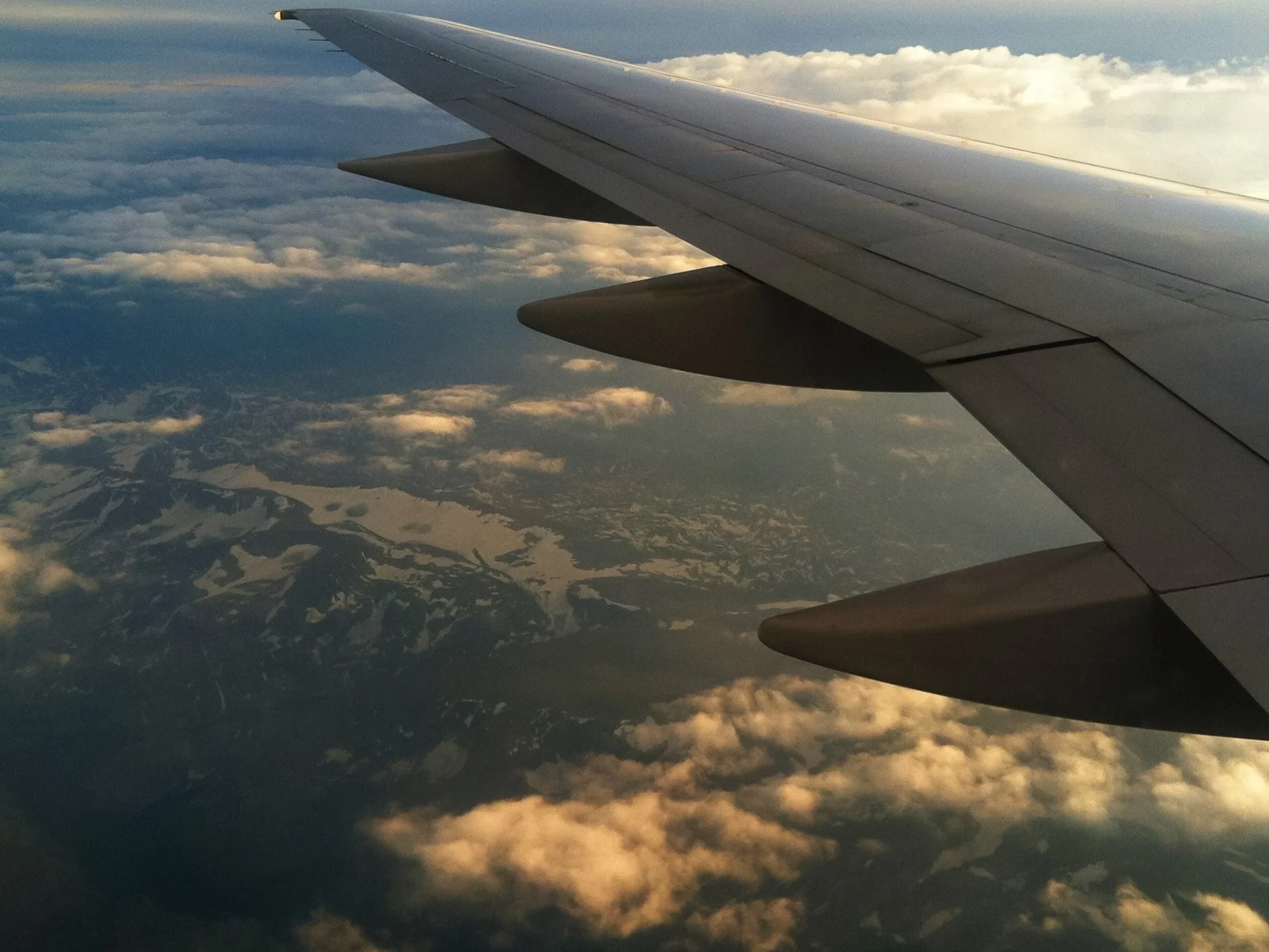 View from an airplane window over clouds and snowy mountains