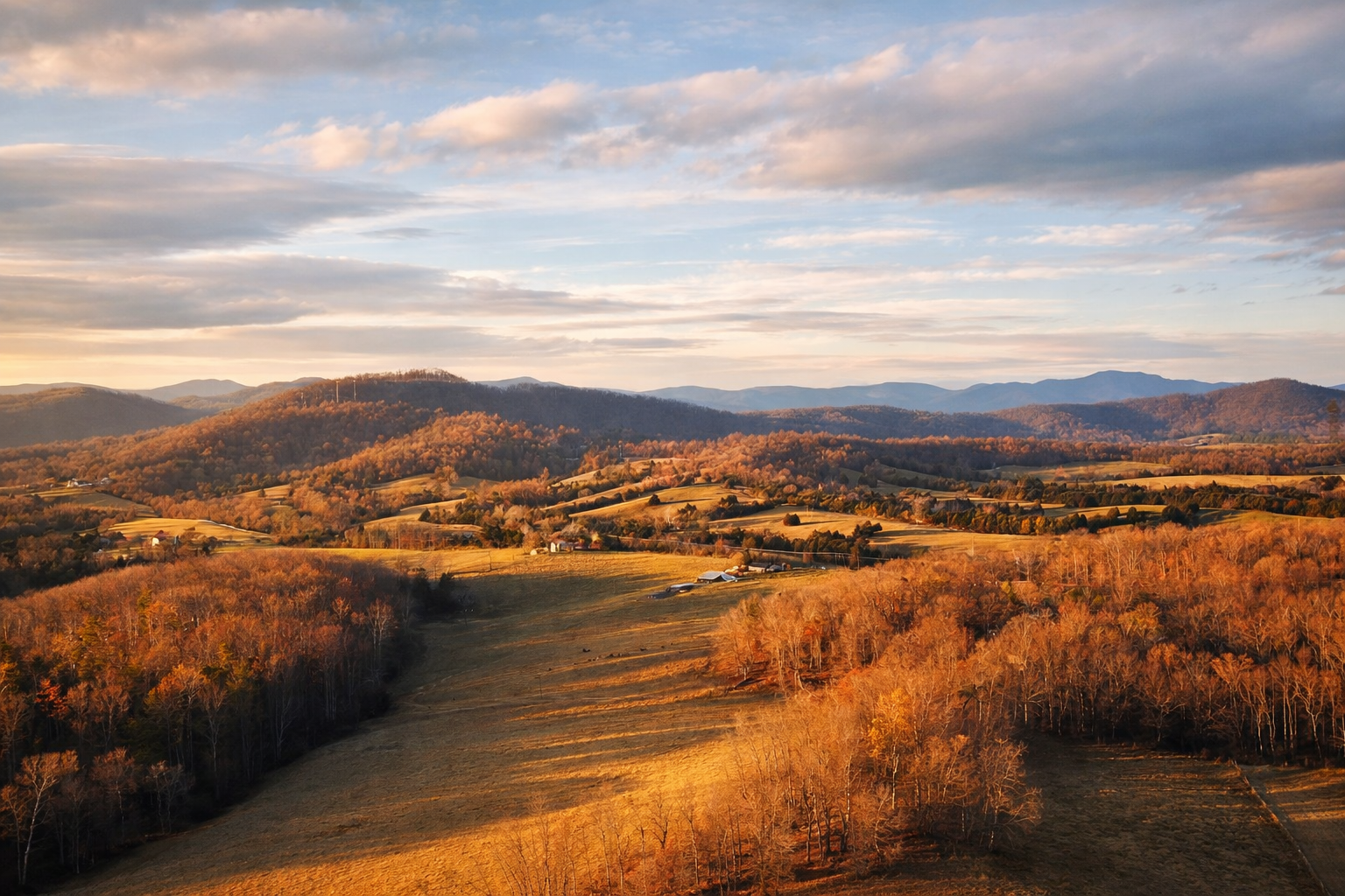 An expansive view of rolling hills and mountains covered in autumn foliage with scattered farmhouses, fields, and forests under a partly cloudy sky.