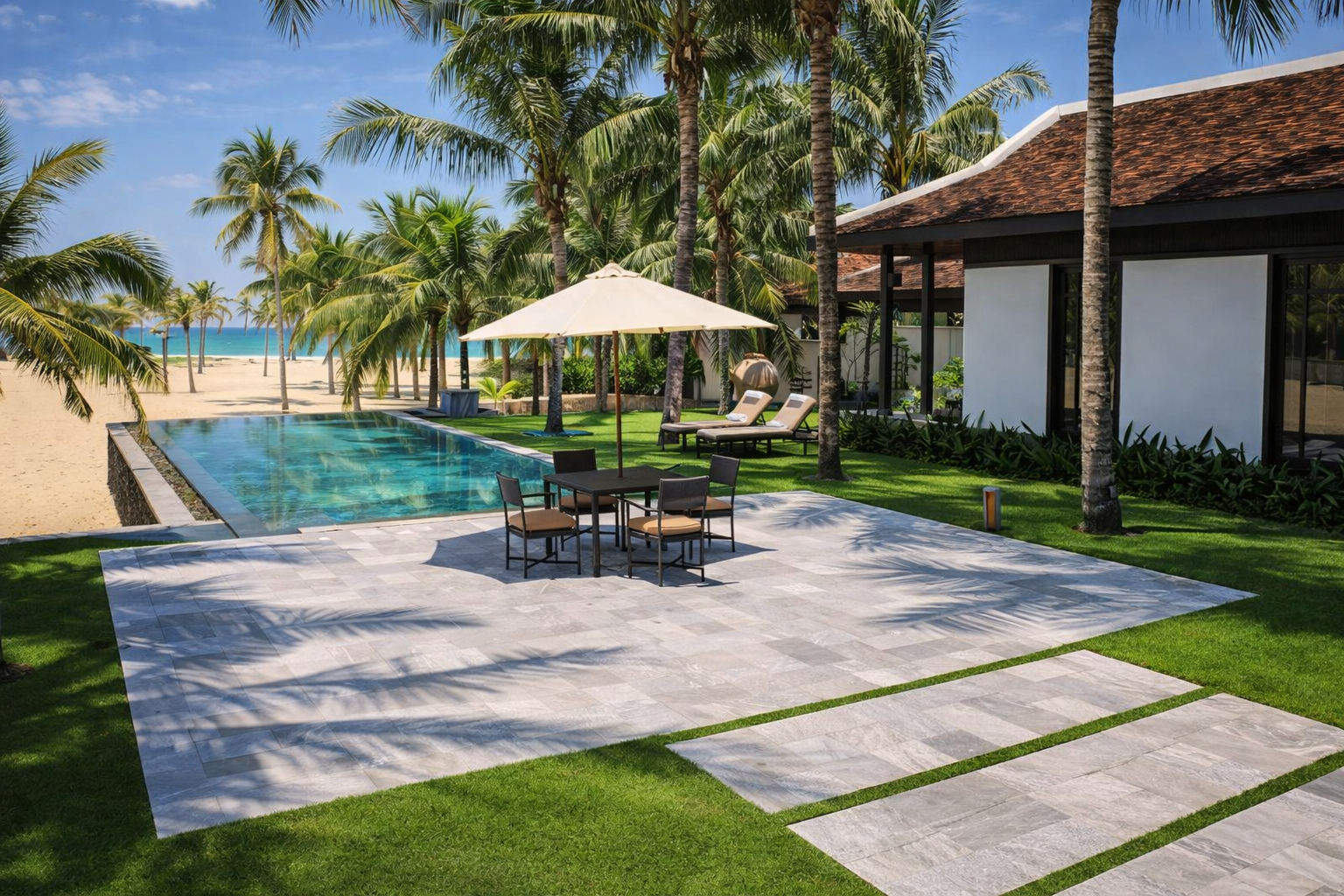 Luxury poolside area at a beach resort with palm trees, a swimming pool, patio furniture with an umbrella, and a building with large windows, overlooking a sandy beach and ocean.