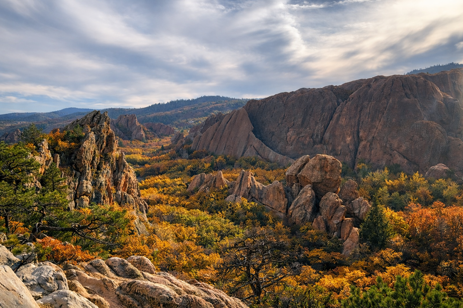 Rocky mountain landscape with autumn foliage in a valley, under a cloudy sky.