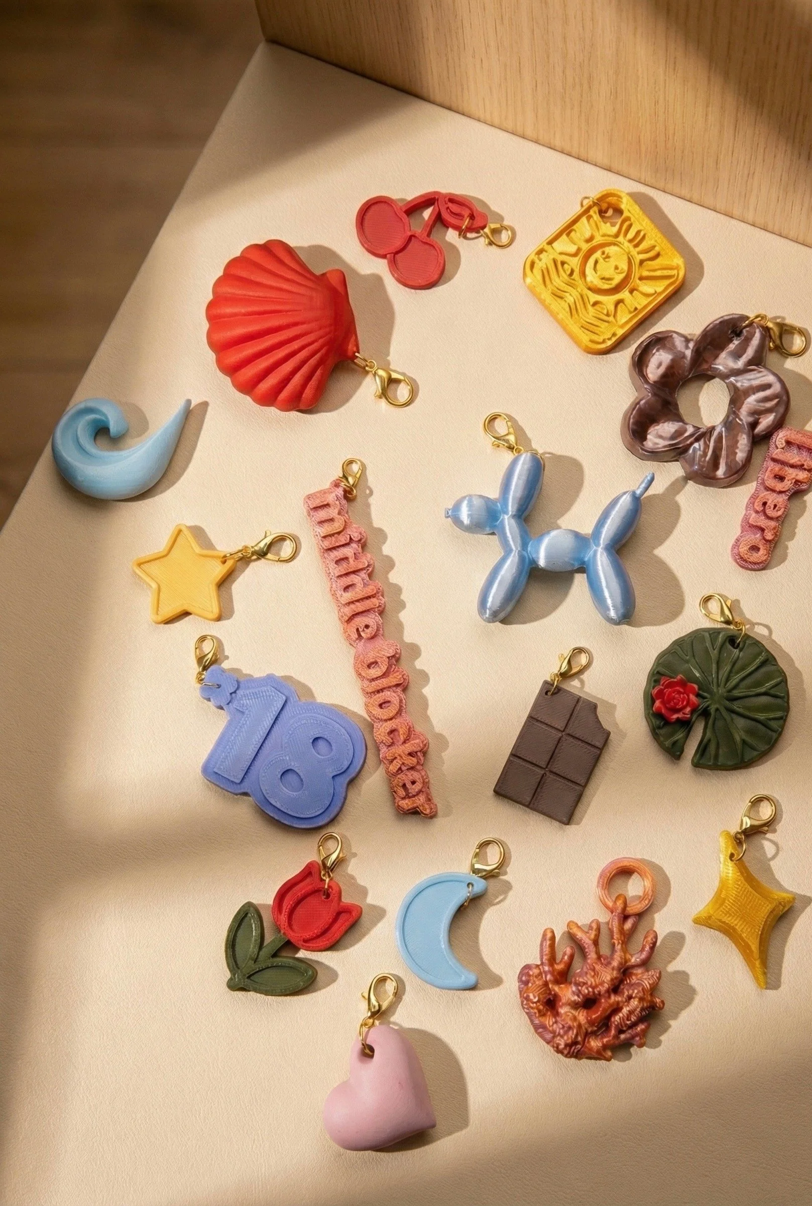 Collection of colorful charms in various shapes including a shell, star, moon, chocolate bar, flower, and heart, spread out on a beige surface.