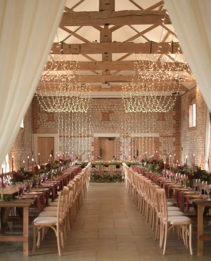 By combining a soft fairy light canopy with rich, seasonal styling, you can create a warm Christmas atmosphere that feels both elegant and inviting. The partition drapes gently define the transition between dining and reception areas, adding depth an