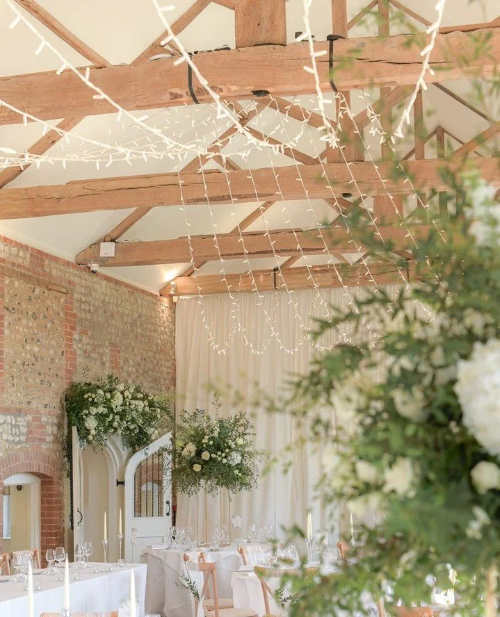 By combining a "Central Apex" scheme with fairy lights, a "Partition Drape" and elegant table styling, a March wedding can feel effortlessly light and fresh. Enhancing the natural tones of the barn while creating a romantic glow f